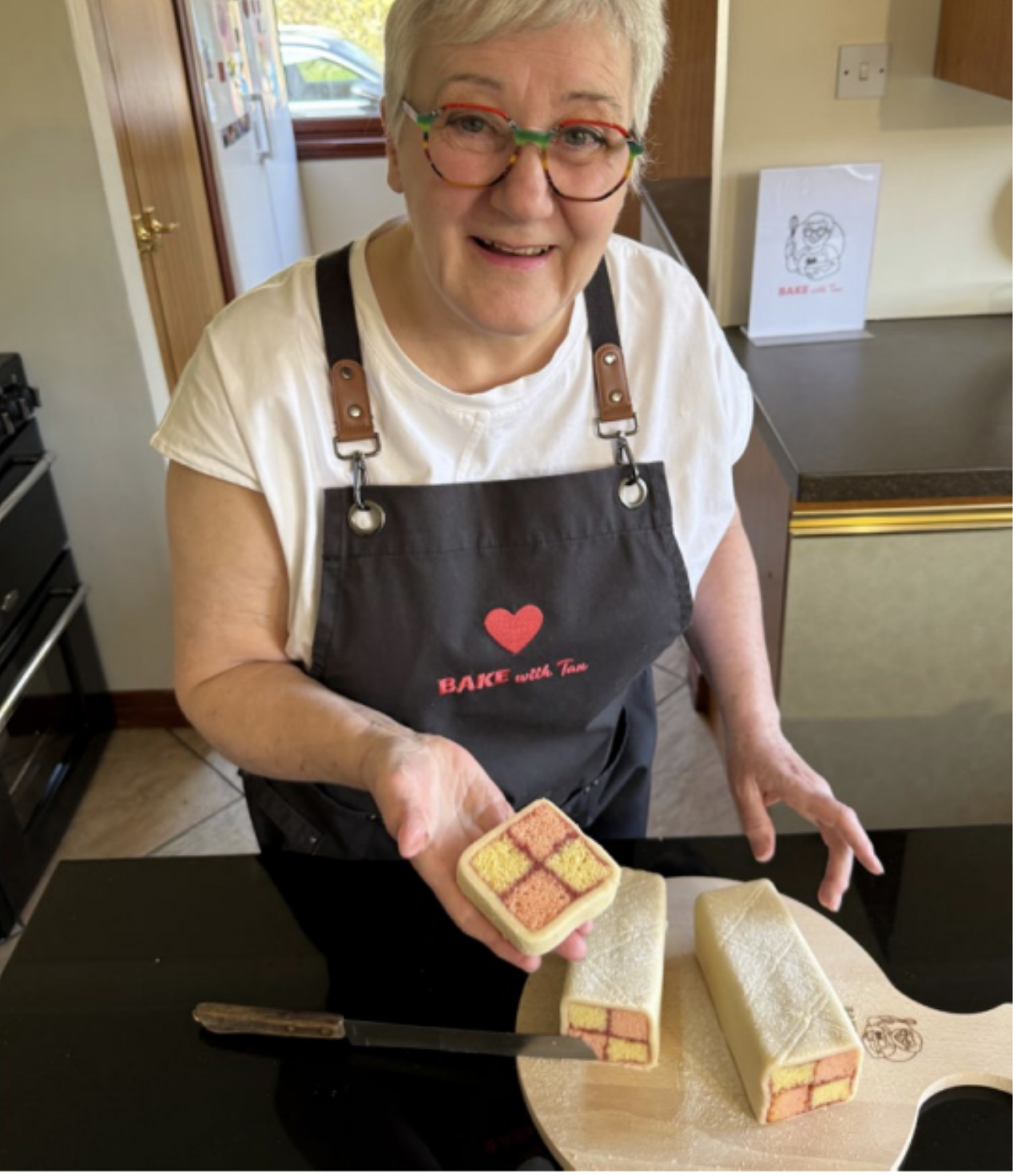 Tan in her kitchen holding a Battenberg cake